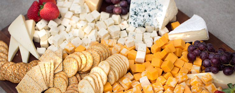 Different types of cheeses and crackers with strawberries and grapes on a wooden platter.